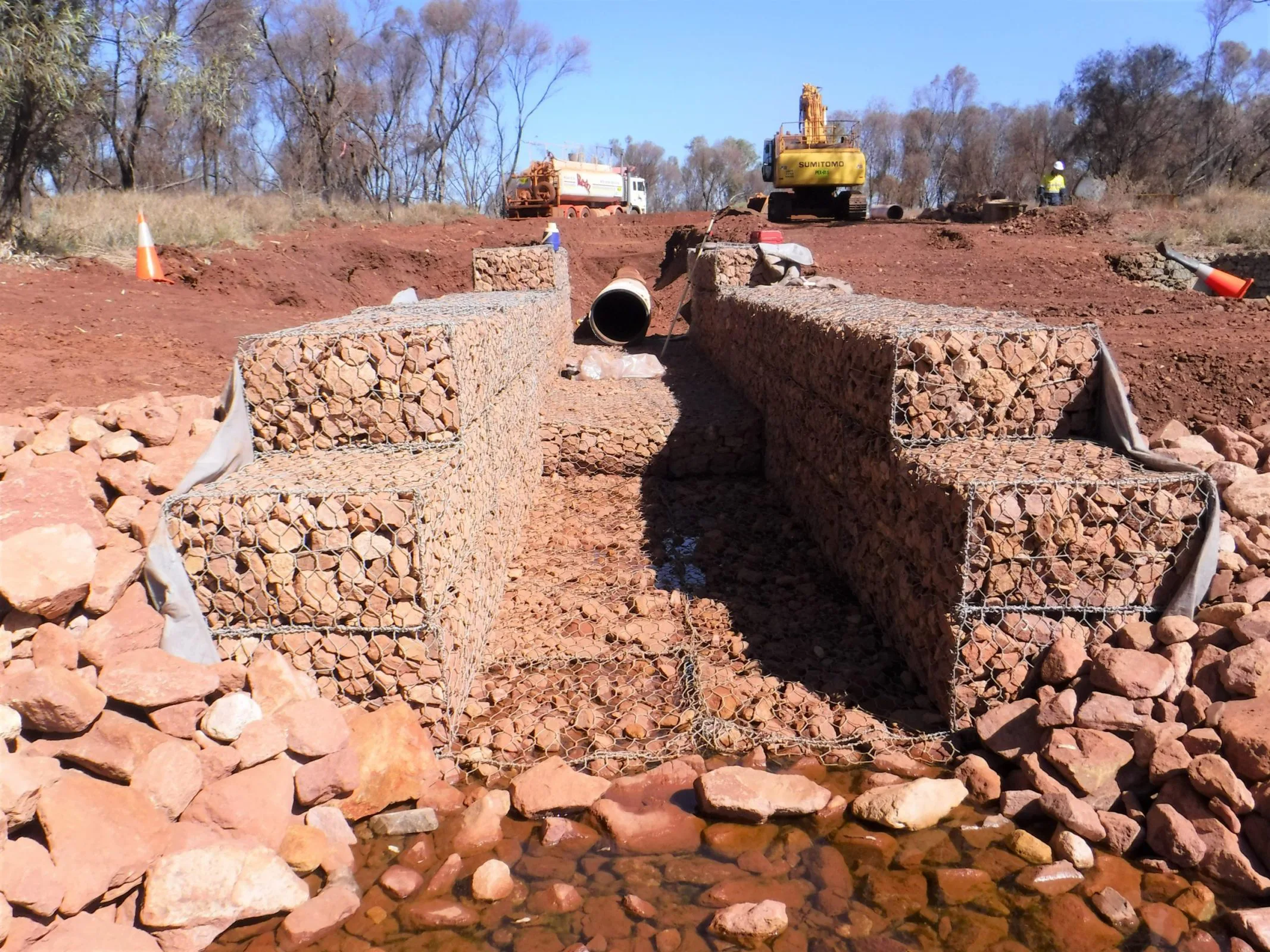 A civil construction image showing a massive rock wall with a pipe embedded within it.