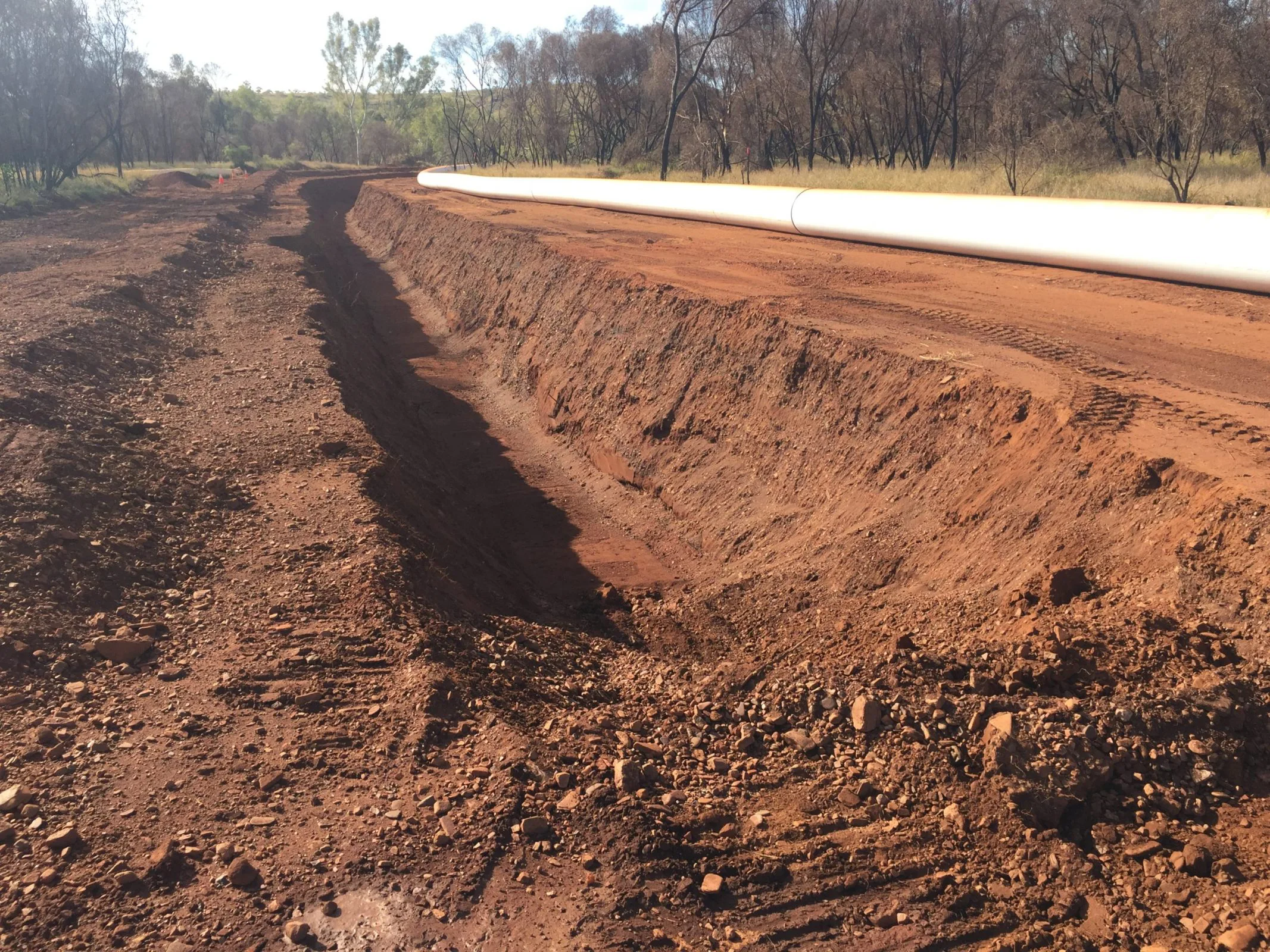 A dirt road with a large trench in the middle, undergoing civil construction work.